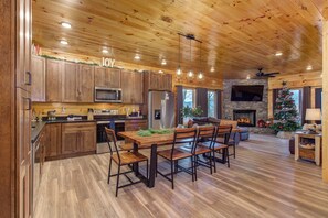 A spacious kitchen with wooden cabinets, a dining area with a wooden table and chairs, a stone fireplace, and a Christmas tree. - 3BD Indoor Pool Cabin Near TOWN | HotTub + FirePit (Sevierville)