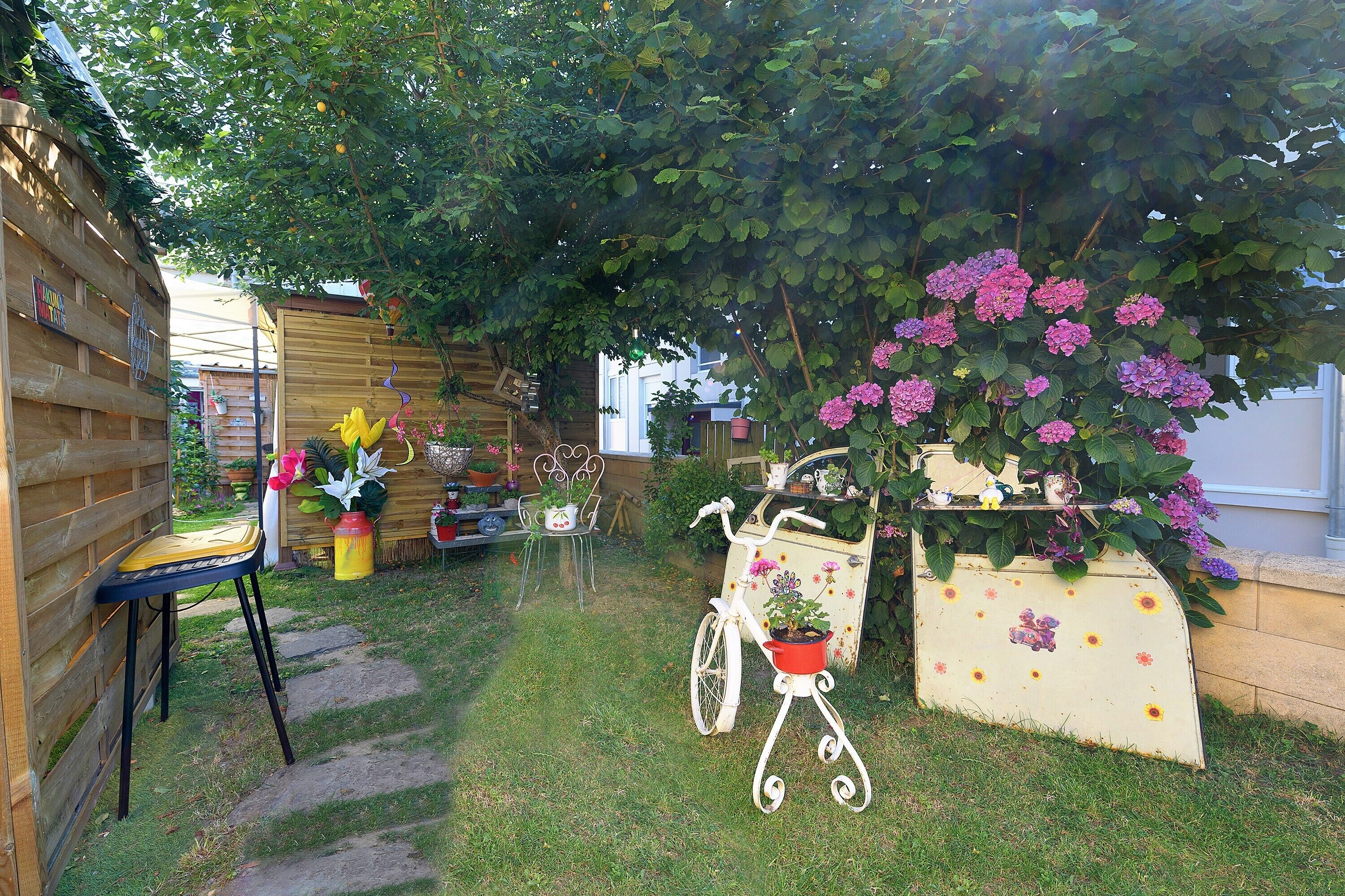 A garden with a wooden fence, a bicycle, and a planter with flowers.