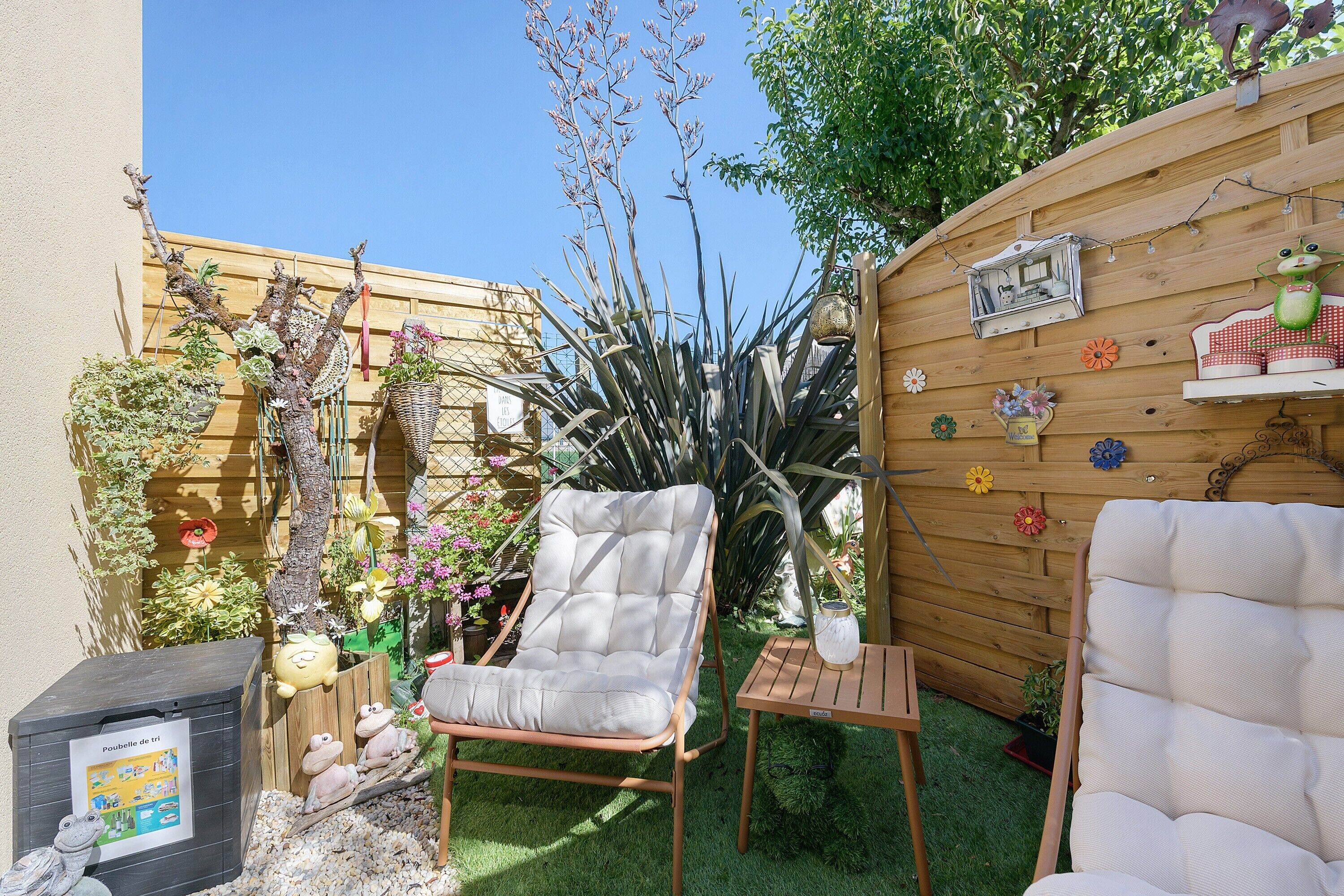 Un jardin avec deux chaises, une petite table, ainsi que diverses plantes et décorations.