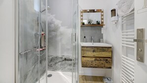 Ein Badezimmer mit Duschkabine aus Glas, Waschtisch mit Spiegel und Beleuchtung sowie Handtuchhalter.
