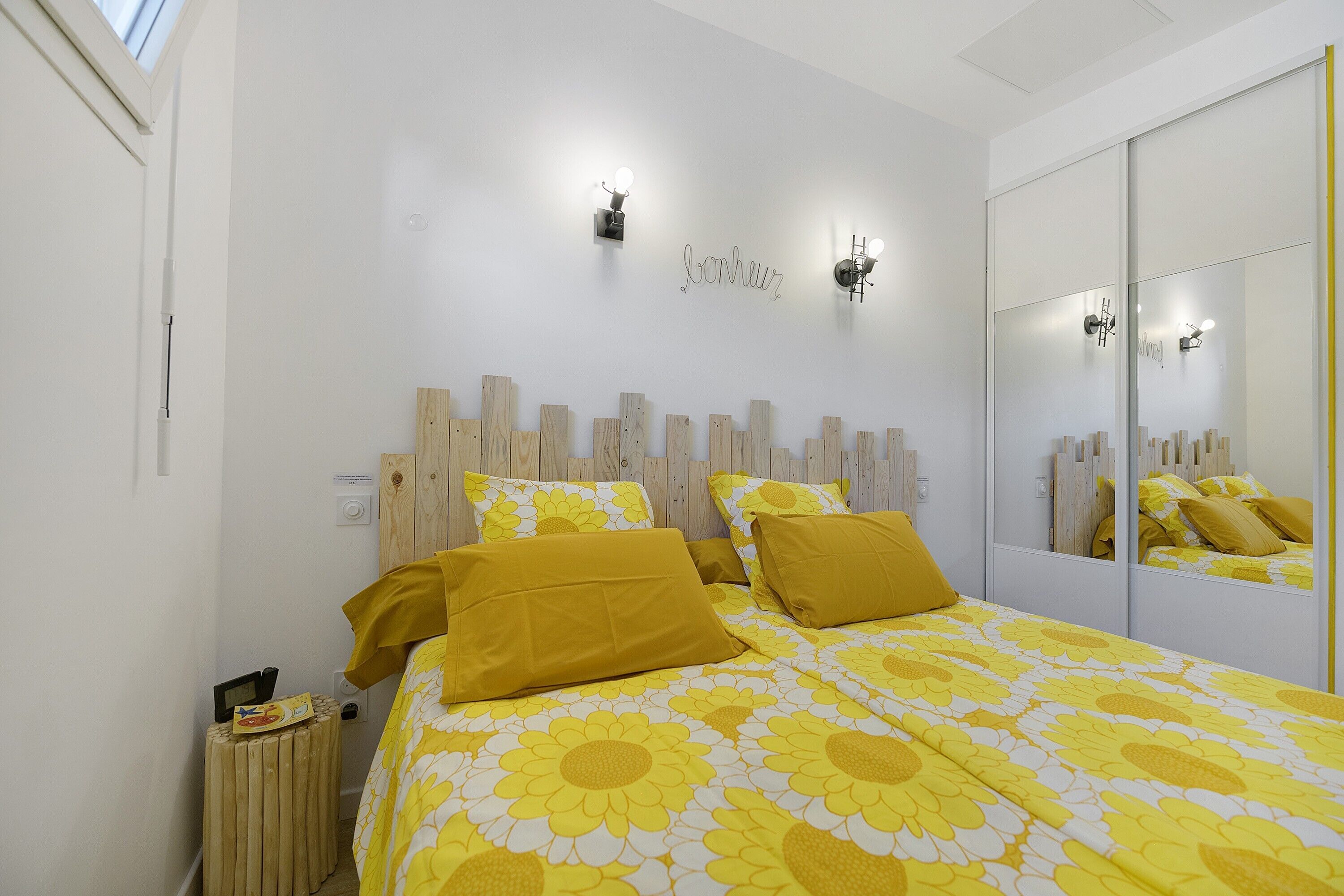 Una camera da letto con un letto, un comodino, uno specchio e una lampada a parete.