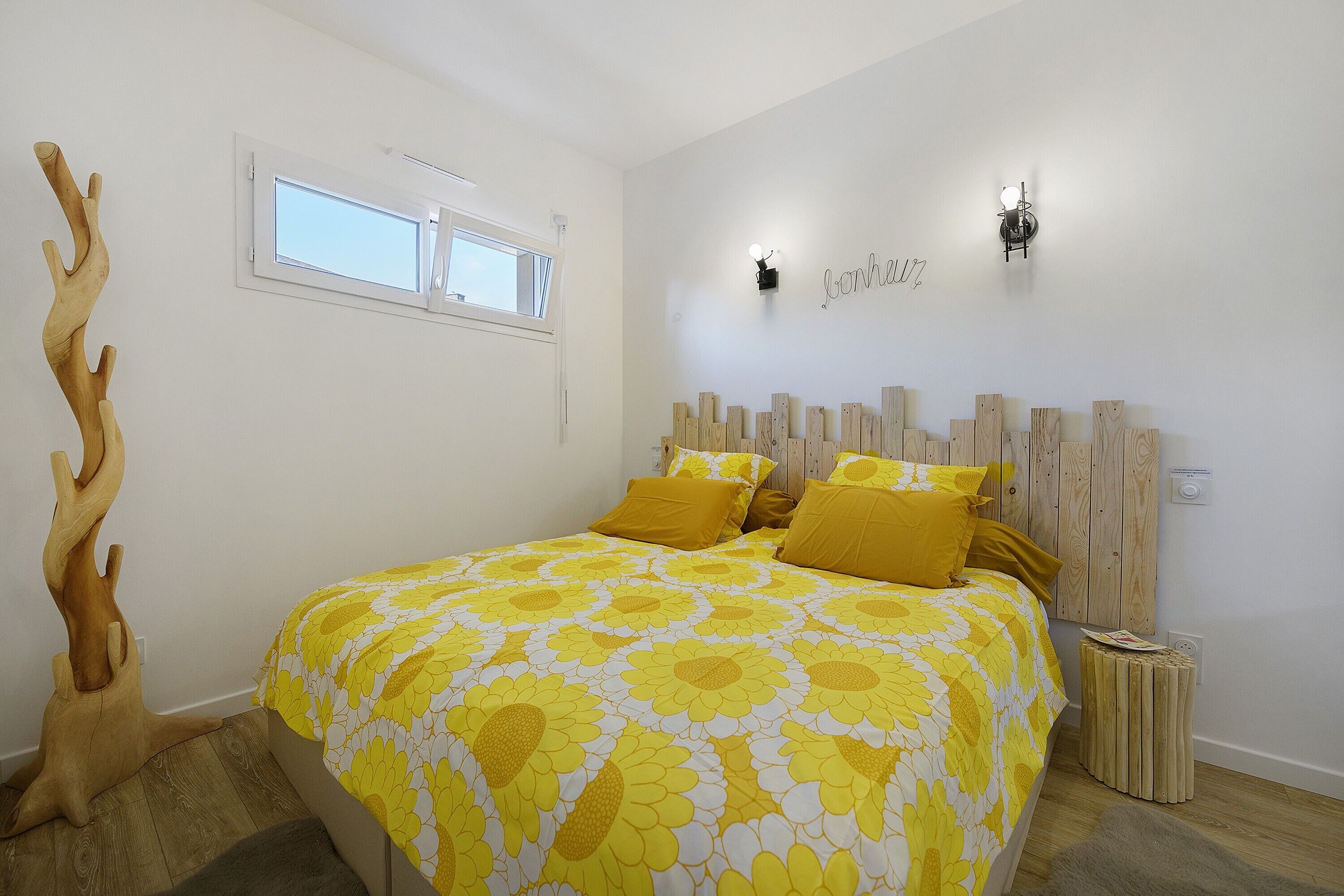 A bedroom with a bed, a wooden headboard, a wall-mounted light, and a window.