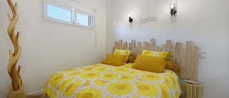 A bedroom with a bed, a wooden headboard, a wall-mounted light, and a window.