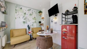 Ein kompakter Wohnraum mit Sofa, Esstisch, einem roten Kühlschrank und einem wandmontierten Fernseher.
