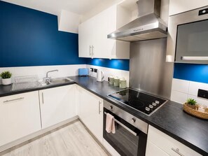 A modern kitchen with white cabinets, a black countertop, stainless steel appliances, and a blue accent wall. - York Centre Flat - balcony, lift & 2 baths (York)