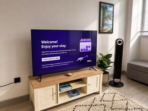 A television displaying a welcome message with a check-out date selection option, a Roku logo, and a wooden entertainment unit with books and a plant. - York Centre Flat - balcony, lift & 2 baths (York)