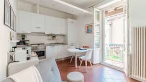 Una cucina moderna con mobili bianchi, un tavolo da pranzo con sedie, un divano e vista sul balcone esterno.