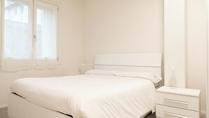 Un dormitorio blanco con cama, mesita de noche y cómoda.