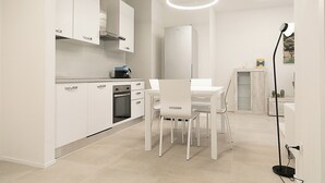 Una cocina moderna con armarios blancos, horno integrado y una zona de comedor con sillas y mesa blancos.