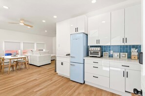 A modern kitchen with white cabinets, a blue refrigerator, and a dining area with a white table and chairs. - La Jolla Villa - Steps to Windansea (San Diego)