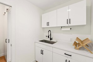 Eine moderne Küche mit weißen Schränken, einem schwarzen Wasserhahn und einem Wäscheständer aus Holz.