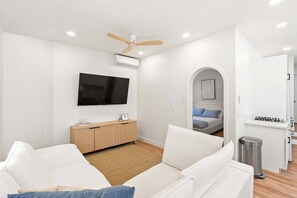 Een moderne woonkamer met een witte bank, een tv die aan de muur is bevestigd, een houten kast en een plafondventilator.