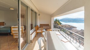 Un balcón con mesa y sillas, una cama y vistas a un lago y montañas.