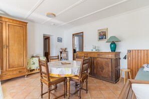 Ein Essbereich mit Holztisch, Stühlen, einem Schrank und einem Bett mit Kopfteil.