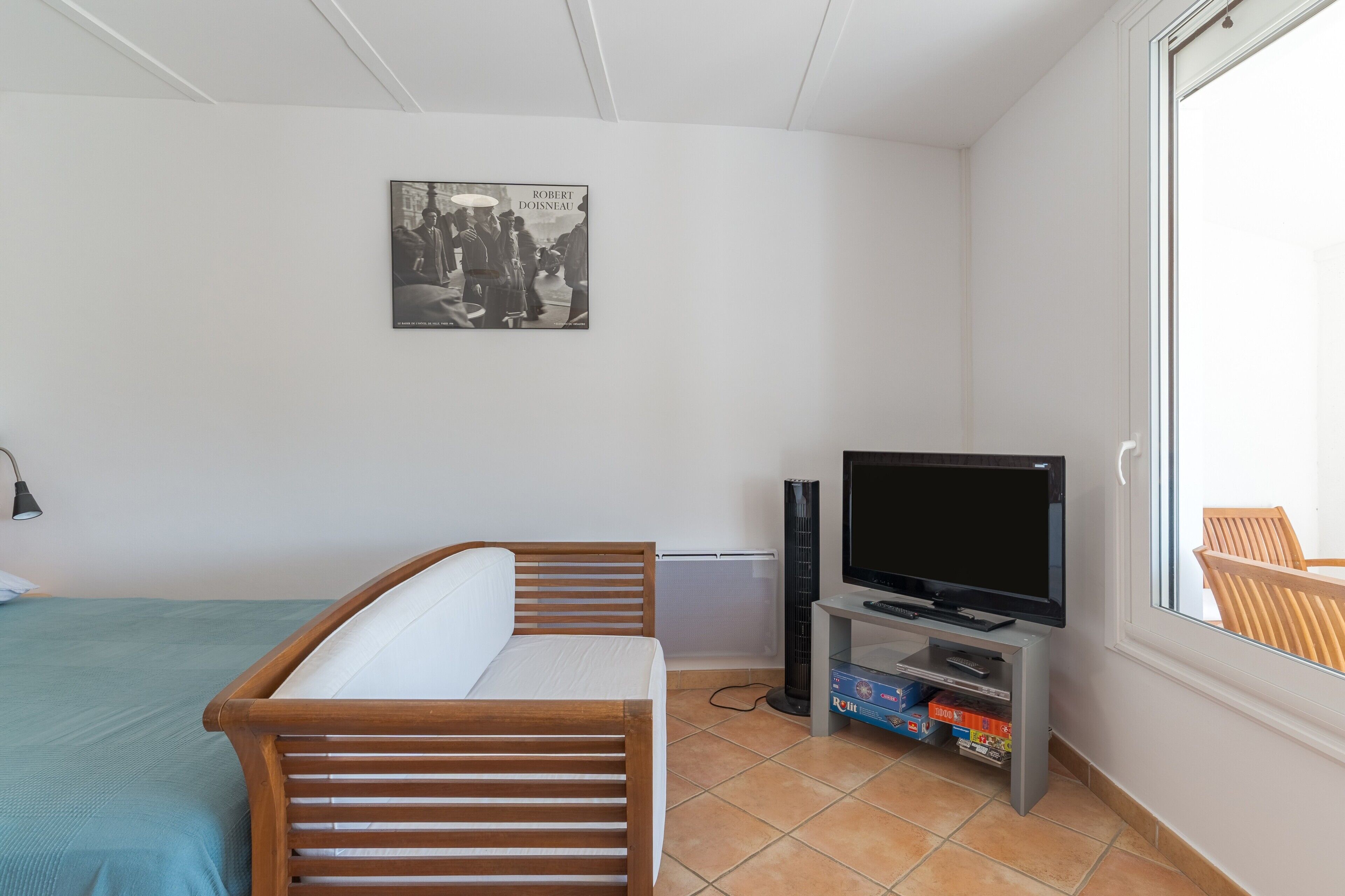 Une chambre à coucher avec un lit, un téléviseur posé sur un meuble, un tableau accroché au mur et une fenêtre.