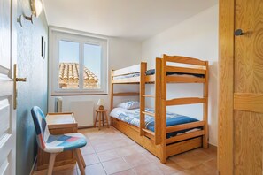 Ein Schlafraum mit Etagenbett, Fenster, Schreibtisch und Stuhl.