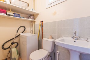 Ein Badezimmer mit Toilette, Waschbecken, Staubsauger und einem Regal mit diversen Gegenständen.