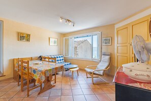 Ein gemütliches Zimmer mit Esstisch, Stühlen, einer Couch, einem Ventilator und einem Fenster mit Blick auf ein Gebäude.
