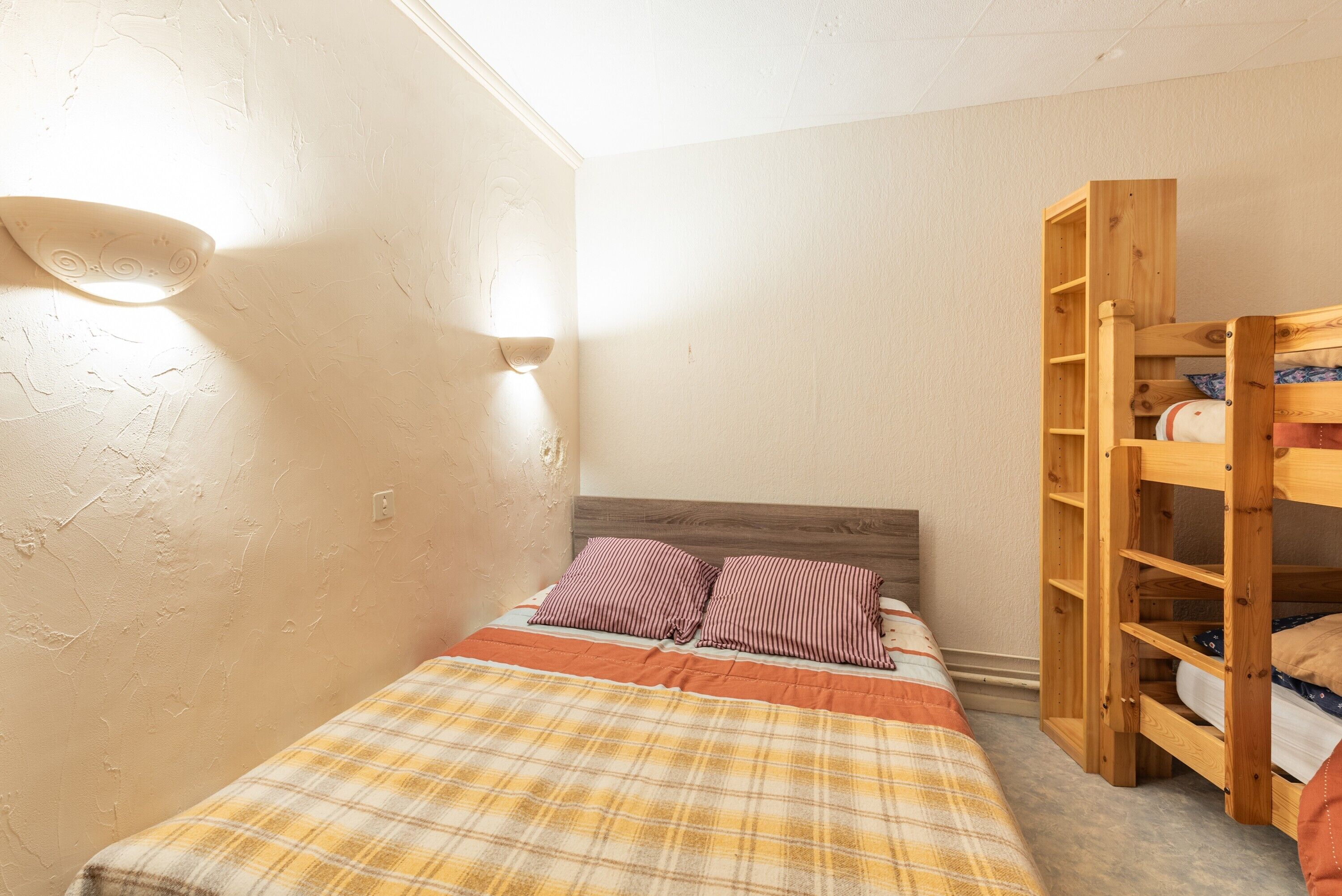 A small bedroom with a single bed, a wooden wardrobe, and a wall-mounted light fixture.