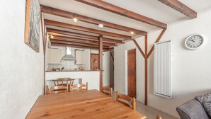 A wooden dining table with chairs, a kitchen in the background, and a clock on the wall.