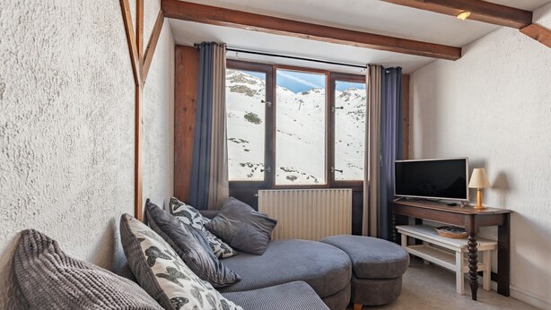 A cozy living room with a sectional sofa, a television, and a view of a snowy mountain.