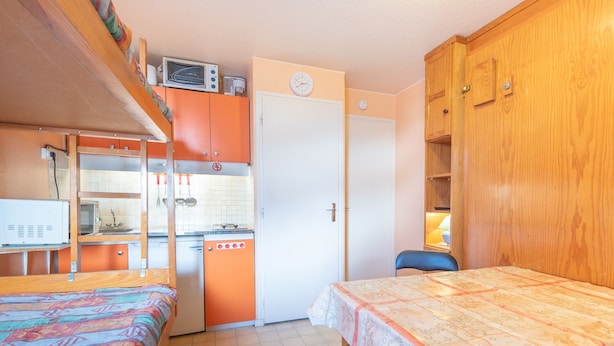 Ein kleines Zimmer mit Stockbetten, einer Küchenzeile, einem Einzelbett mit gemustertem Bettbezug und einem Holzschrank.
