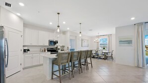 Een moderne keuken met witte kastjes, een centraal eiland met barstoelen en een eetgedeelte met uitzicht.
