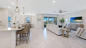 Een modern interieur met een keuken, een eethoek en een zitkamer, met een groot raam en een plafondventilator.