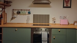 Keittiössä on vihreät kaapit, ruostumattomasta teräksestä valmistettu uuni, seinälle ripustettu teline mukeille ja laatoitettu välitila.
