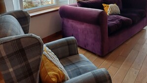 Olohuoneessa on suuri ikkuna, kaksi ruutukuosisia nojatuolia, violetti sohva ja keltainen koristetyyny.