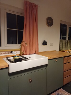 Eine Küche mit einem weißen Spülbecken, grünen Schränken, einer Holzarbeitsplatte und einem Fenster mit Vorhang.