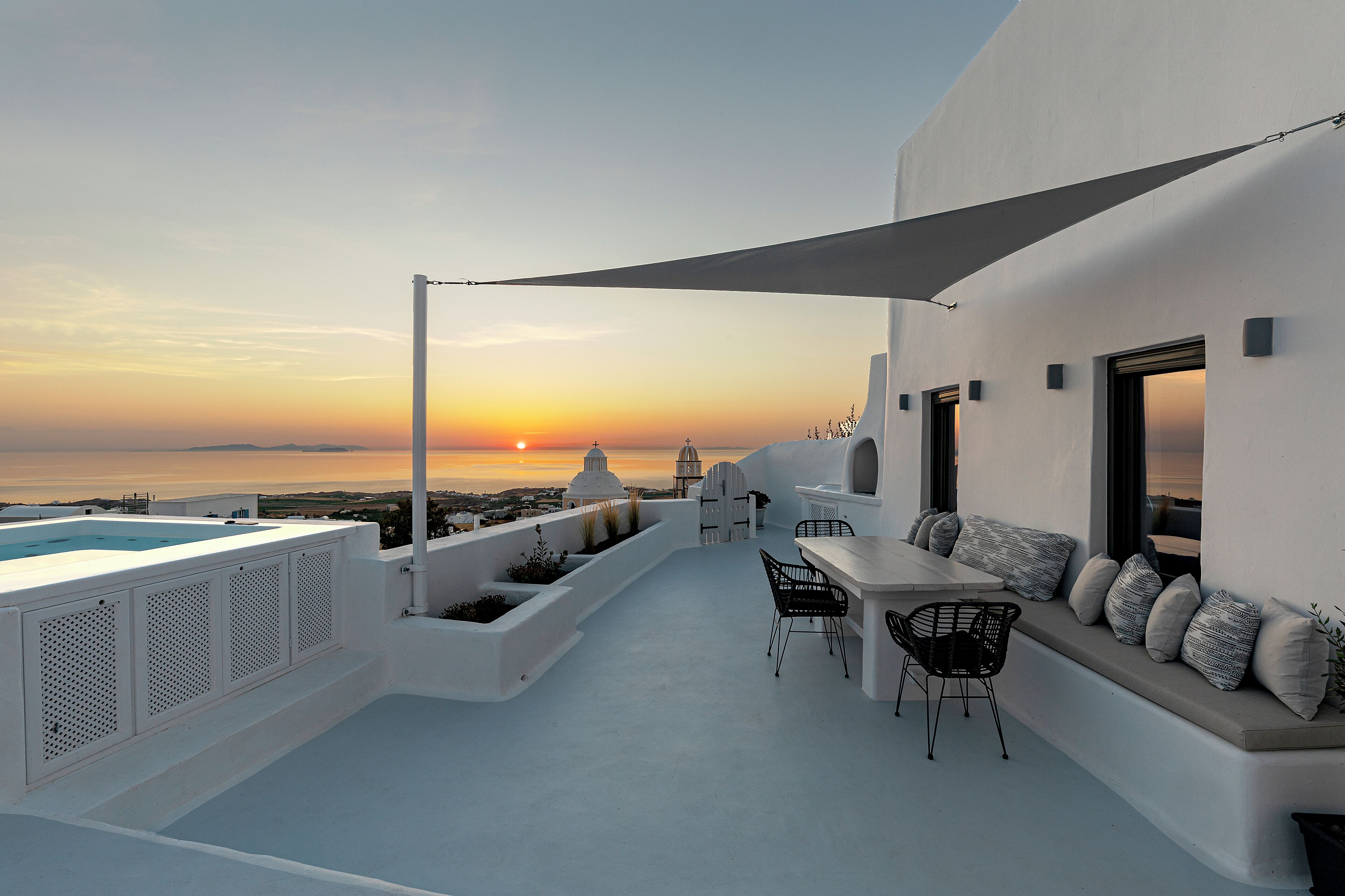 A rooftop terrace with a pool, seating area, and a view of the sunset over the sea.