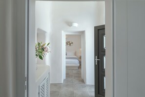 A hallway leading to a bedroom with a bed, a wall-mounted light fixture, and a decorative wall piece. - Aleanna Traditional Villa Fira   (Fira)