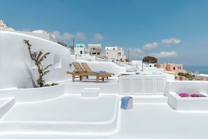 Un edificio de paredes blancas con piscina, sillones de descanso y vista al mar.