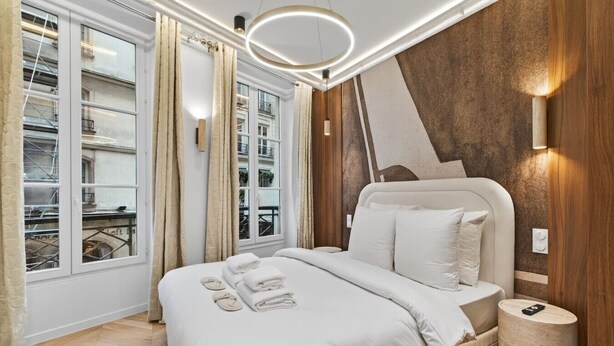 A modern bedroom with a large bed, a wooden accent wall, and a view of the city through large windows. - New suite 6 personnes- Saint Germain Notre-Dame (Paris)