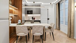 A modern kitchen with a dining area, featuring a white countertop, wooden cabinetry, and a built-in microwave. - New suite 6 personnes- Saint Germain Notre-Dame (Paris)