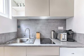 Una cocina moderna con un lavamanos de acero inoxidable, una placa vitrocerámica integrada, un tostador y una cafetera.