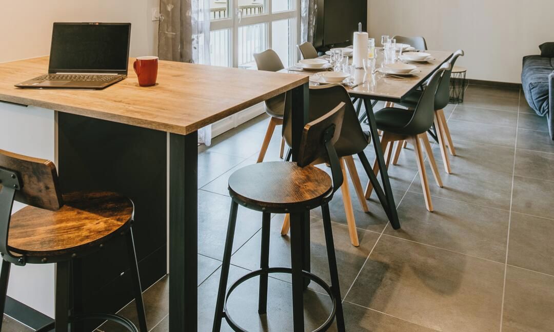 Moderni ruokailutila, jossa on puinen pöytä, mustat tuolit, kannettava tietokone ja punainen muki.