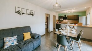 Una sala de estar moderna con un sofá gris, una mesa de comedor preparada para cuatro personas y una cocina al fondo.