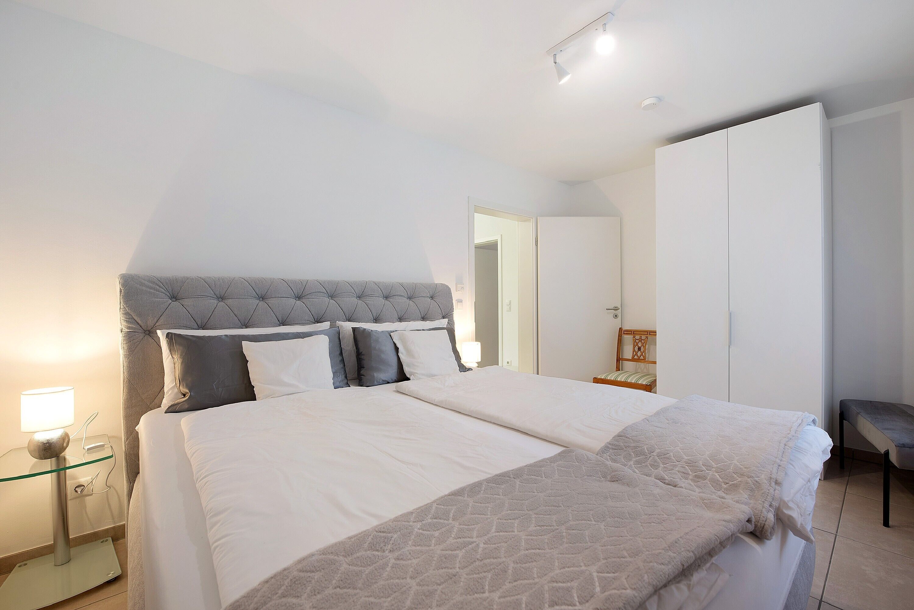 A double bed with a tufted headboard, a bedside table with a lamp, and a bench.