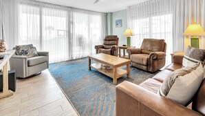 Uma sala de estar com um ventilador de teto, duas poltronas de couro, um sofá, uma mesa de centro e um tapete.