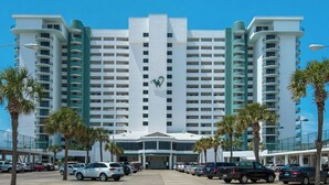 Um hotel de vários andares com um logo 'W' em destaque, apresentando uma entrada central, estacionamento e palmeiras.