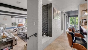 A modern living room with a fireplace, a dining area with bar stools, and a kitchen area. - Luxe Austin Retreat, Pool & Yard, Sleeps 20 (Austin)