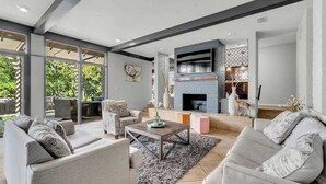 A modern living room with a fireplace, comfortable seating, and a large TV. - Luxe Austin Retreat, Pool & Yard, Sleeps 20 (Austin)