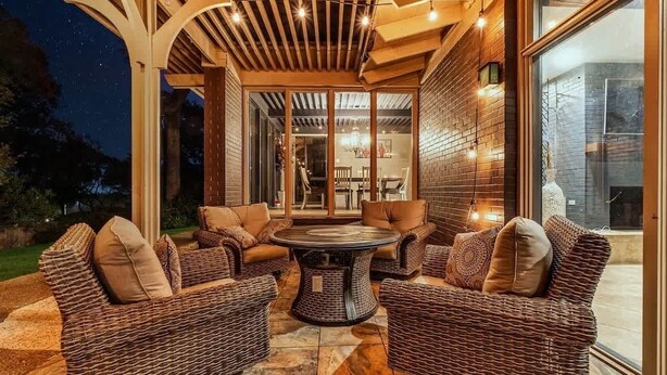 An outdoor patio with wicker furniture, a round table, and a pergola with string lights. - Luxe Austin Retreat, Pool & Yard, Sleeps 20 (Austin)