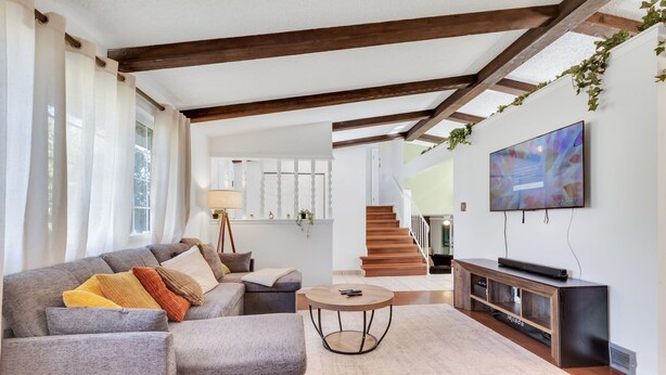 A modern living room with a grey sectional sofa, a round coffee table, and a flat-screen TV on a wooden stand. - 6BD Near DT - BBQ Grill, Games & Football Fun (Arvada)