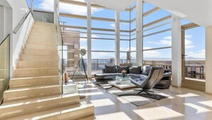 A spacious living area with a high ceiling, large windows, a staircase, and a modern sofa. - Welcome to The Penthouse – Beachfront Luxury (Barcelona)