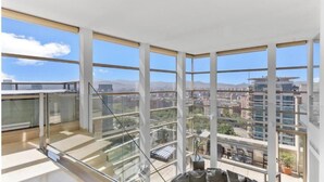 A high-rise apartment with large floor-to-ceiling windows, a glass railing, and a view of a cityscape. - Welcome to The Penthouse – Beachfront Luxury (Barcelona)