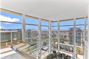 Eine hohe Wohnung mit Panoramafenstern, einer Glasreling und Blick auf eine Stadtlandschaft.