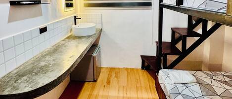 A compact kitchen with a built-in TV, a window with blinds, a sink, and a wooden floor.